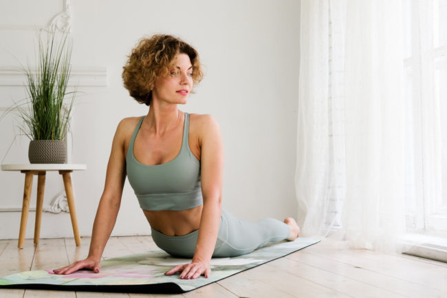 A young, beautiful, woman works out at home on a yoga mat.